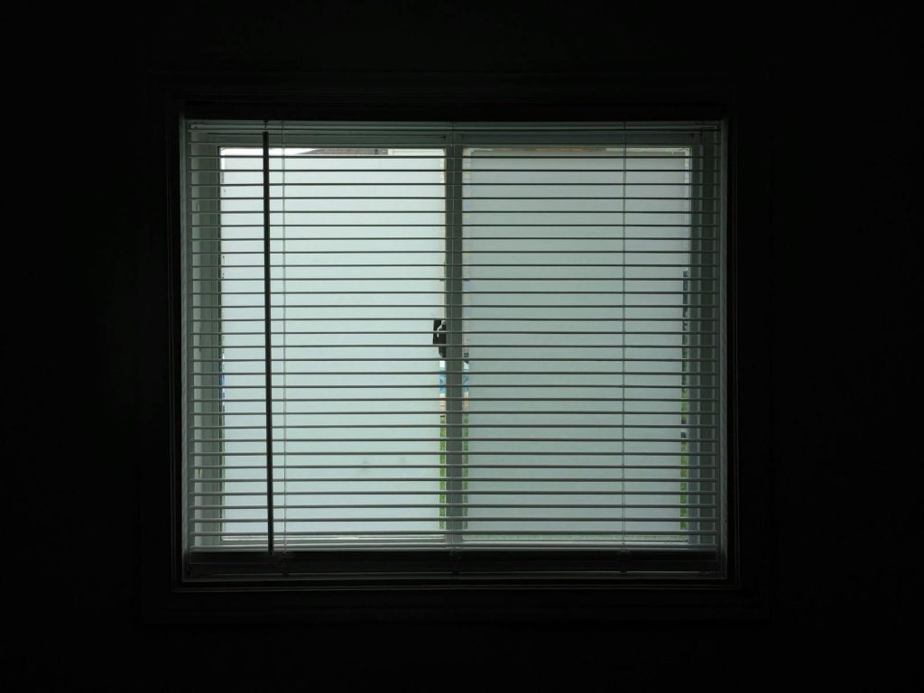 A dimly lit room with closed window blinds casting shadows, creating a serene and secluded atmosphere.