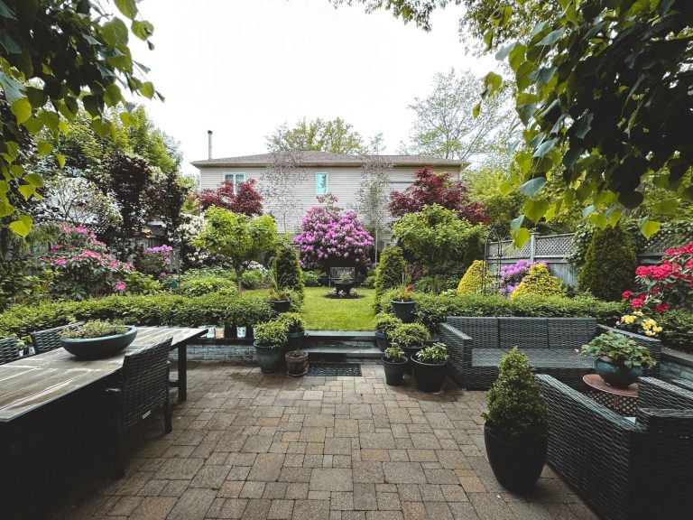 A tranquil backyard garden showcasing vibrant flowers, lush greenery, and patio furniture.