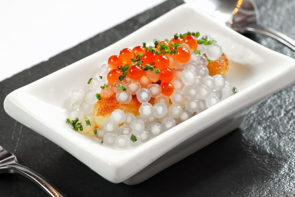 Close-up of a gourmet dish featuring vibrant caviar and translucent tapioca pearls, elegantly plated.