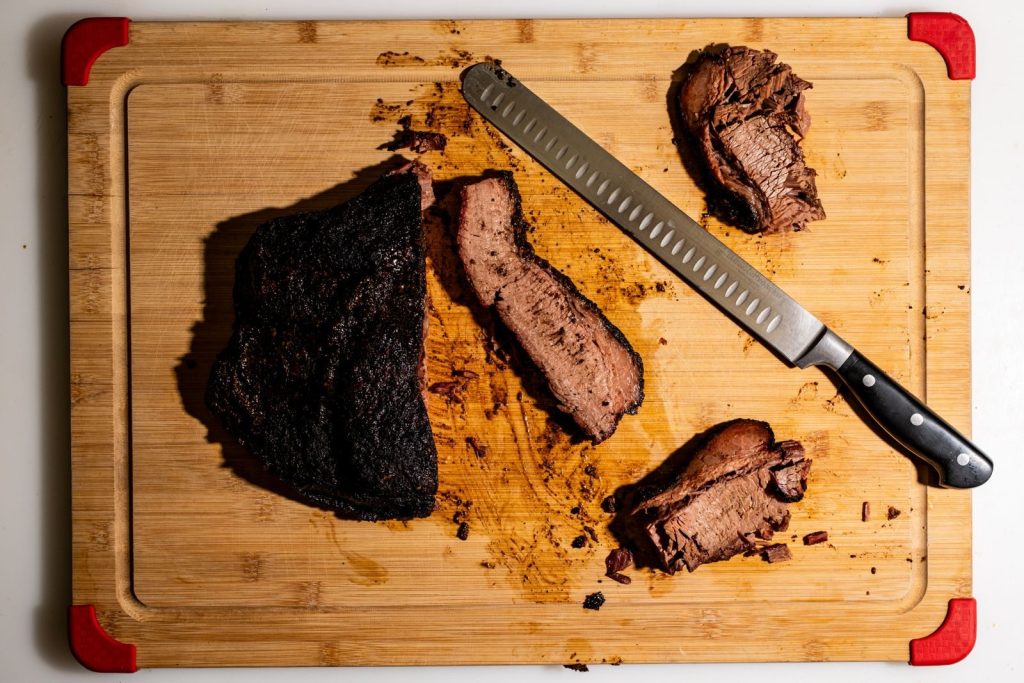 Juicy sliced brisket on a wooden cutting board with a sharp kitchen knife.
