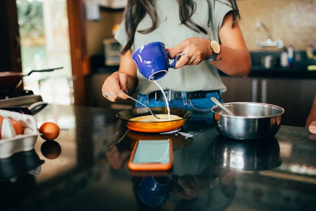 A woman pours milk into a frying pan, preparing breakfast in her modern kitchen.
