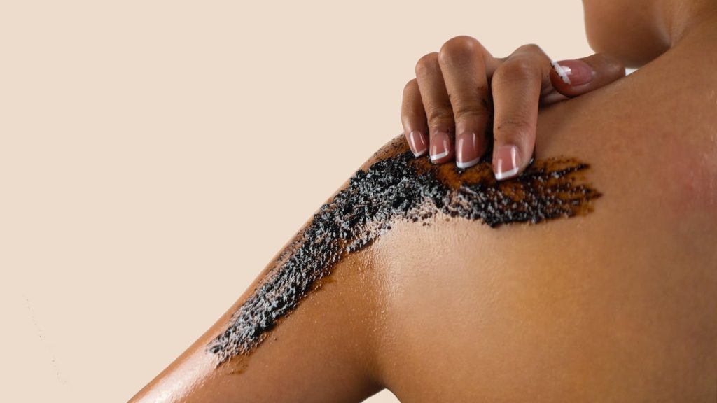 Close-up of a woman applying exfoliating scrub on her shoulder, showcasing beauty and skincare.