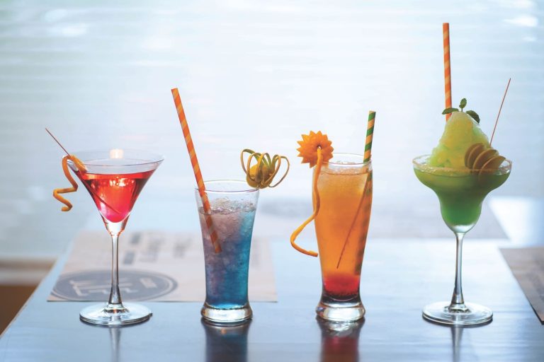 A vibrant assortment of cocktails with straws and garnishes on a bar table, perfect for summer refreshment.