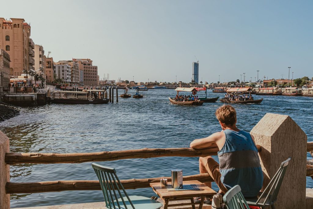 A tranquil scene of Dubai Creek with traditional boats and a relaxed waterfront cafe view.