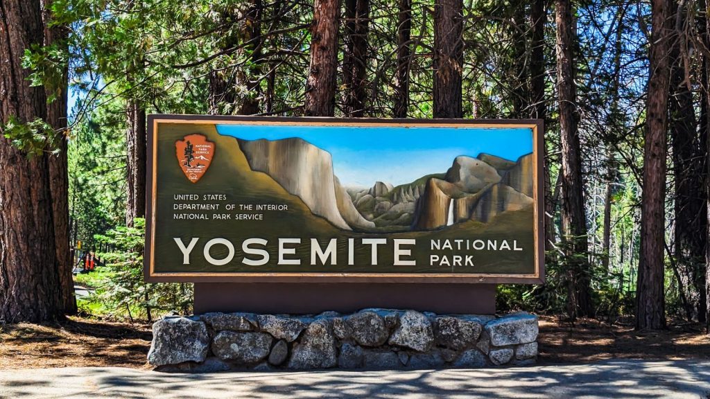 Yosemite National Park entrance sign set against a backdrop of towering trees.