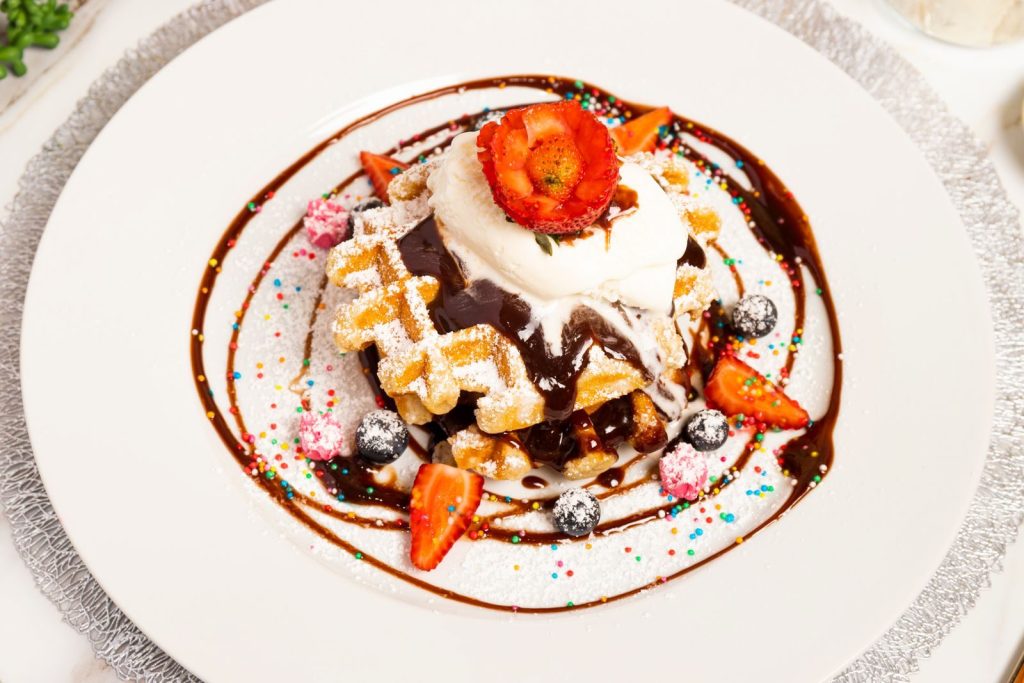 Mouthwatering waffle topped with whipped cream, chocolate sauce, strawberries, and blueberries.