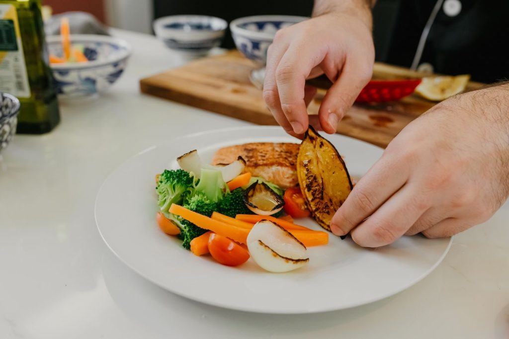 Chef carefully plating grilled salmon with vegetables, showcasing culinary art.