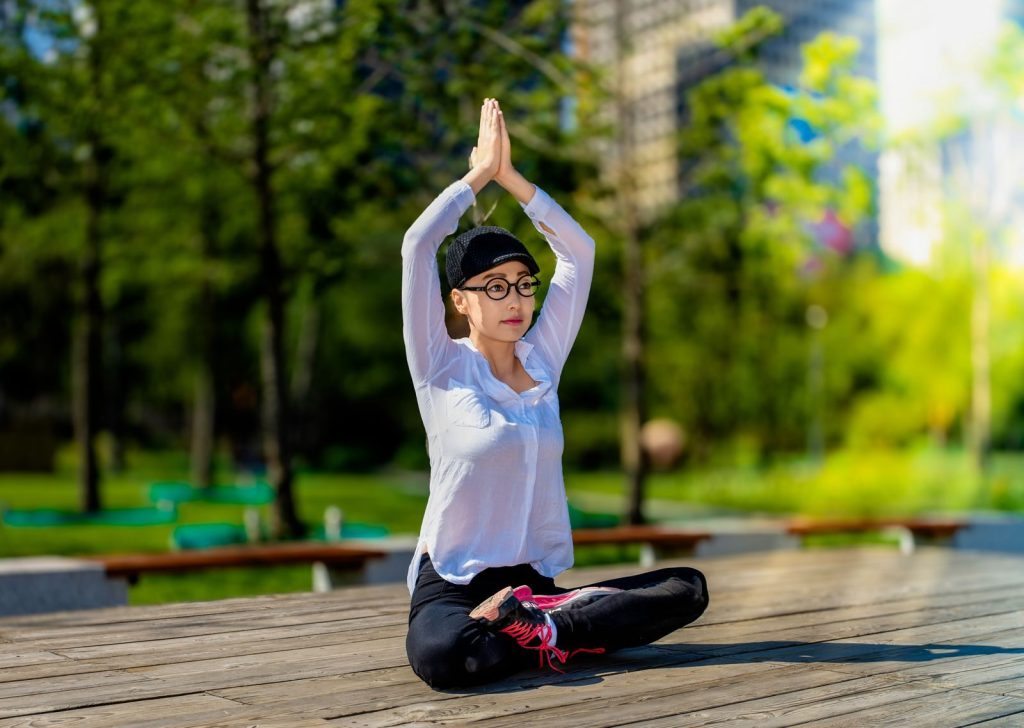 A woman in a white shirt and cap practices yoga outdoors, enhancing mind and body wellness.