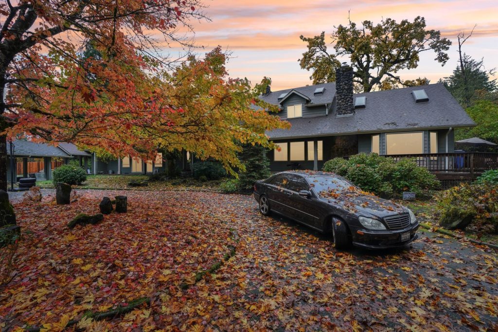 A cozy home surrounded by vibrant fall foliage and a car covered in leaves, creating a serene autumn atmosphere.