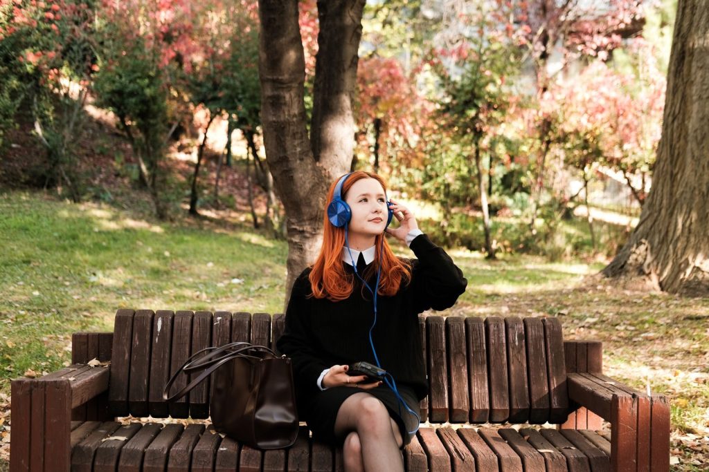 Woman with headphones enjoying music on a park bench during a sunny autumn day.