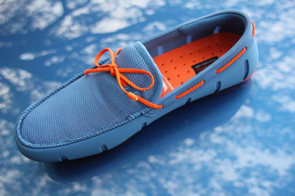 Stylish blue loafer with orange laces on a reflective sky-patterned surface for modern fashion appeal.