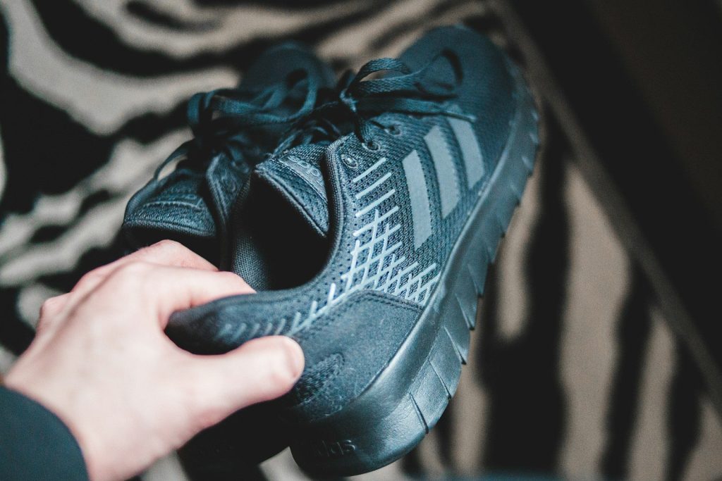 black Adidas running shoes held above black and white carper