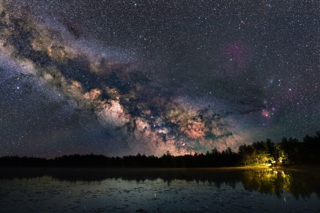 Captivating view of the Milky Way galaxy reflecting over a serene lake surrounded by trees at night.