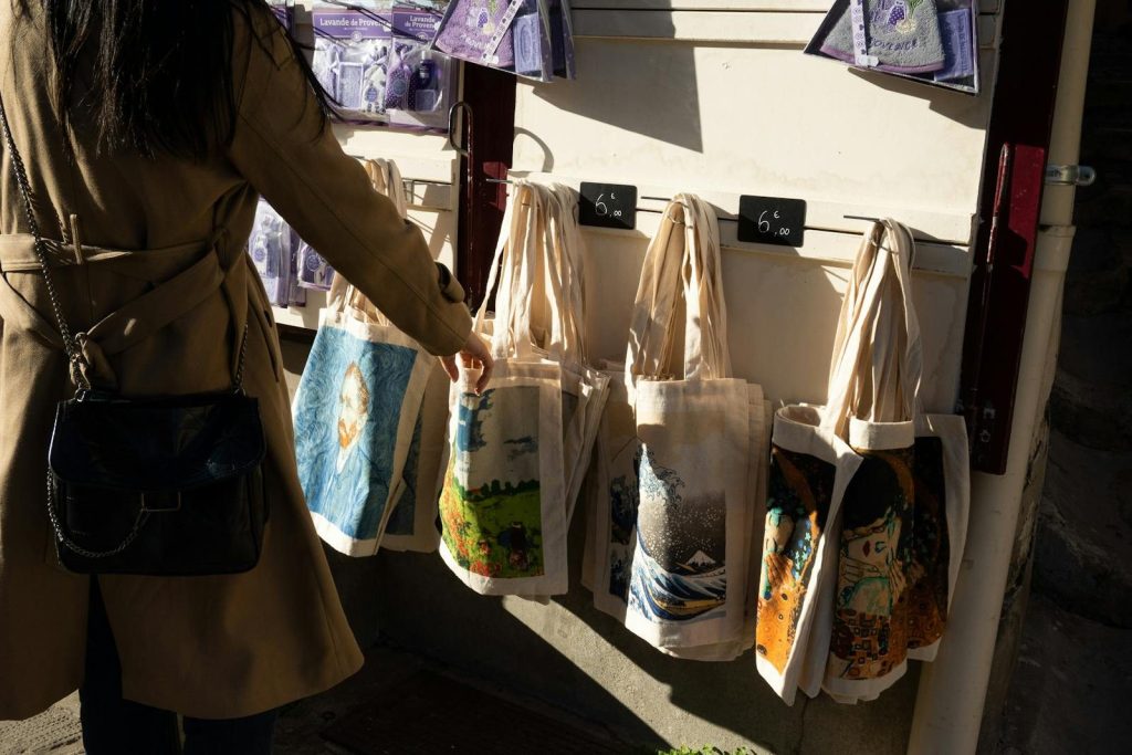 A woman shopping for artistic tote bags at a street market in Arles, France.