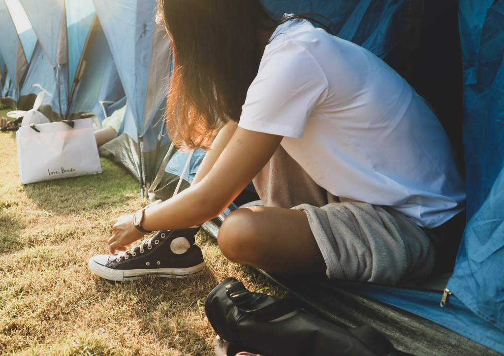 Side view of unrecognizable female in casual outfit sitting near tent and tying shoelaces during festival on sunny summer day