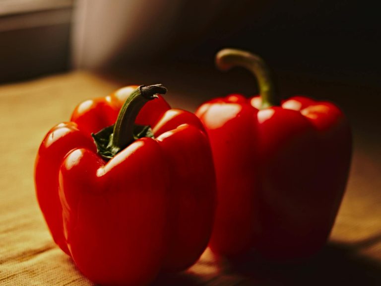 Close-up of vibrant red bell peppers on a wooden table with natural lighting.