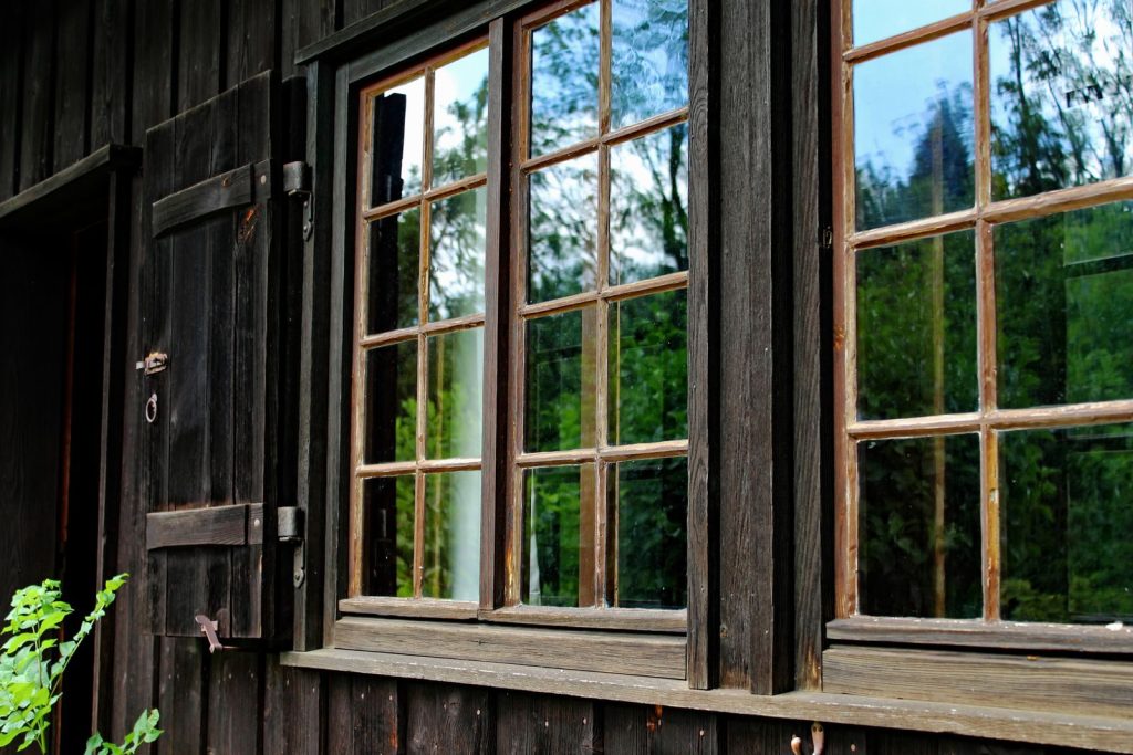 Close-up of a rustic wooden cabin window reflecting lush greenery in Oberstdorf, Bavaria.