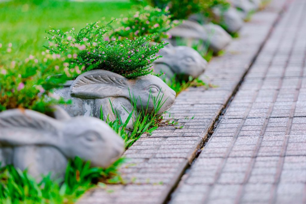 Concrete rabbit planters with flowers line a brick pathway in a vibrant garden setting.