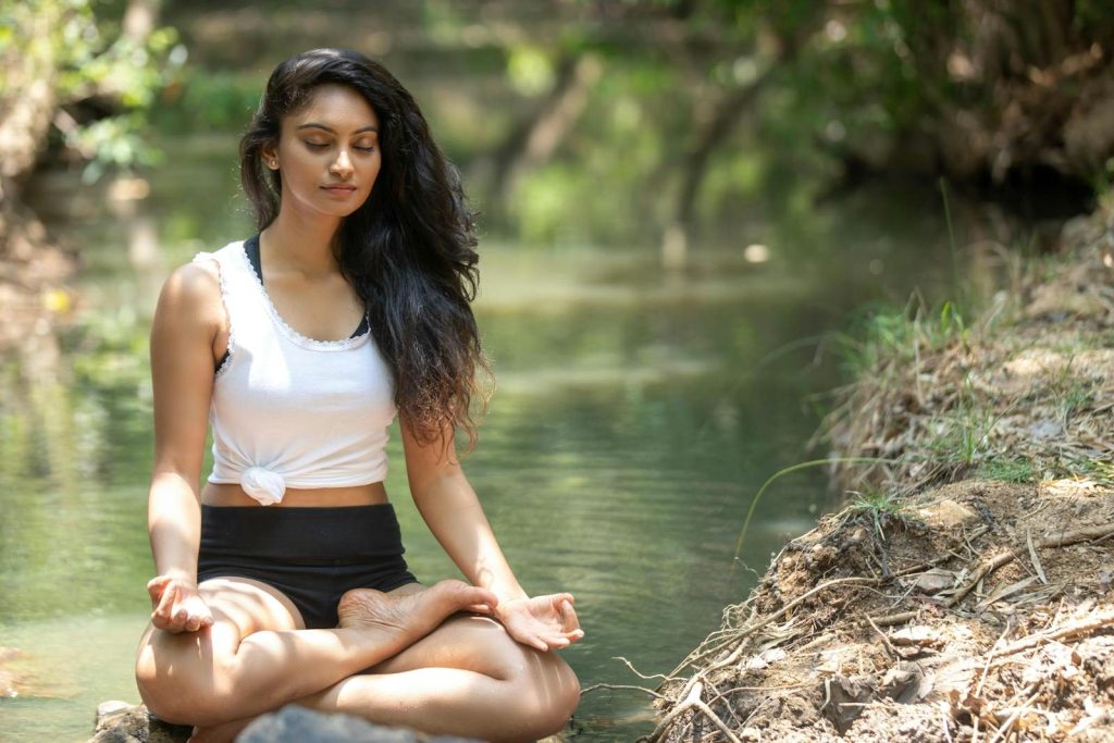 A serene scene of a woman meditating beside a peaceful river in nature.