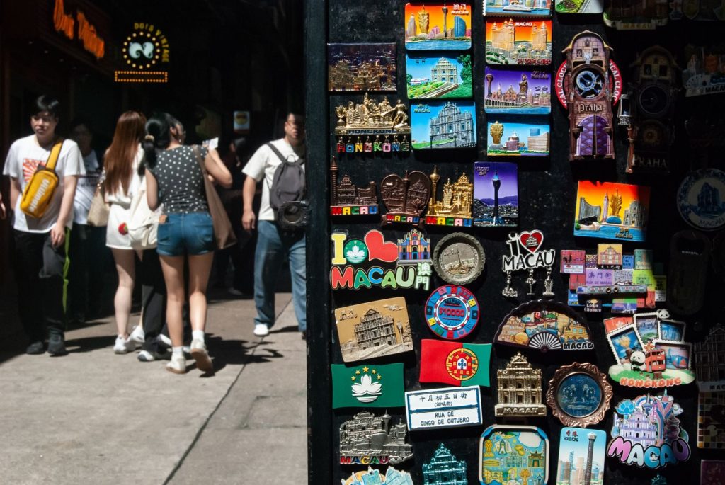 Vibrant collection of Macau-themed souvenirs with pedestrians on a sunny street.