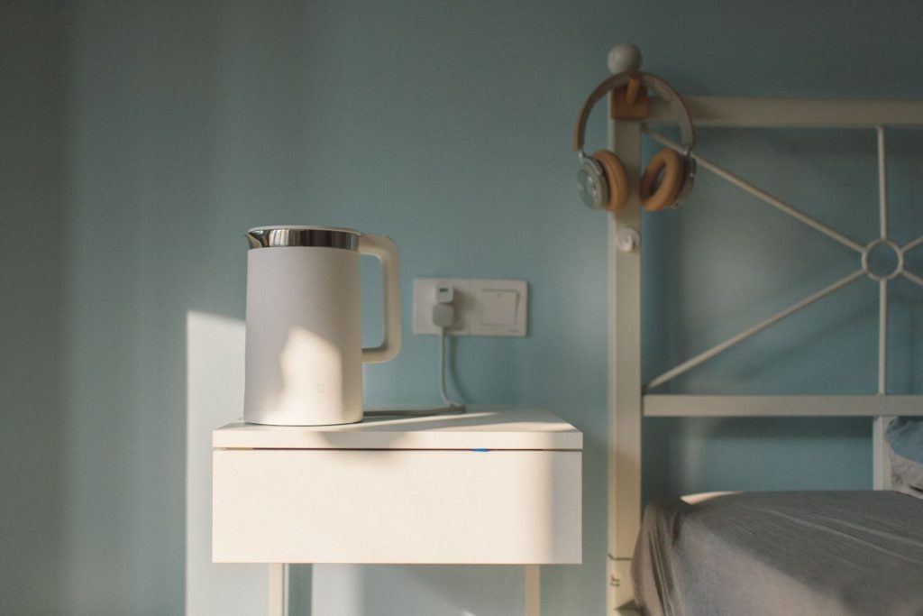 A serene minimalist bedroom scene featuring a white bedside table and a kettle.
