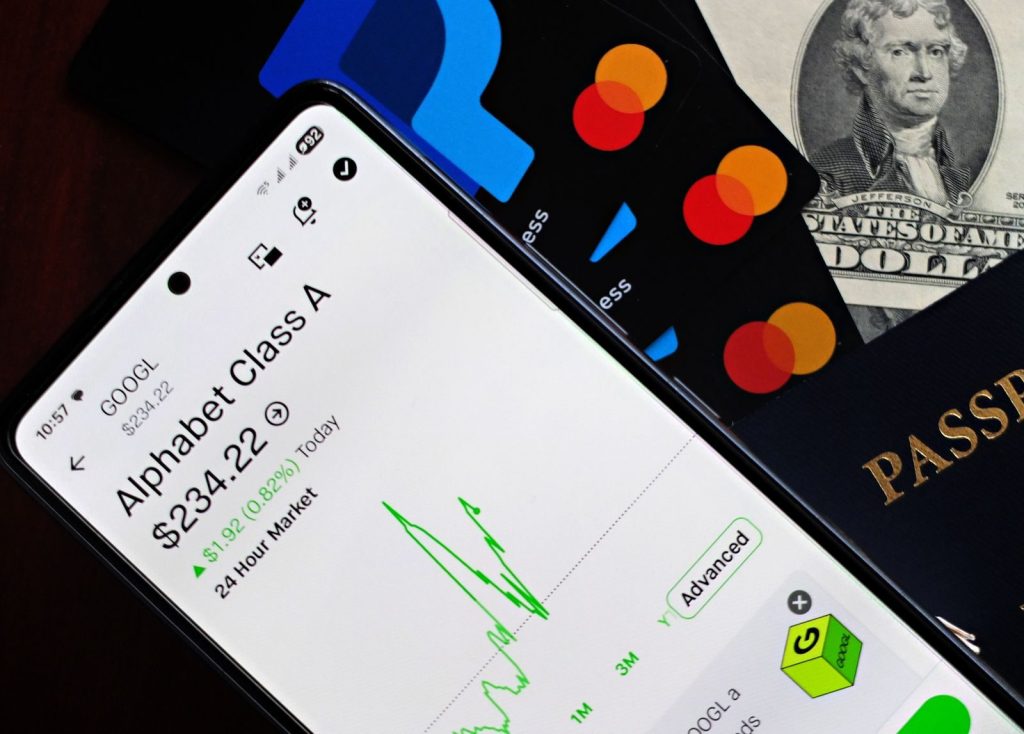 A smartphone displaying Alphabet stock price alongside credit cards, cash, and passport.