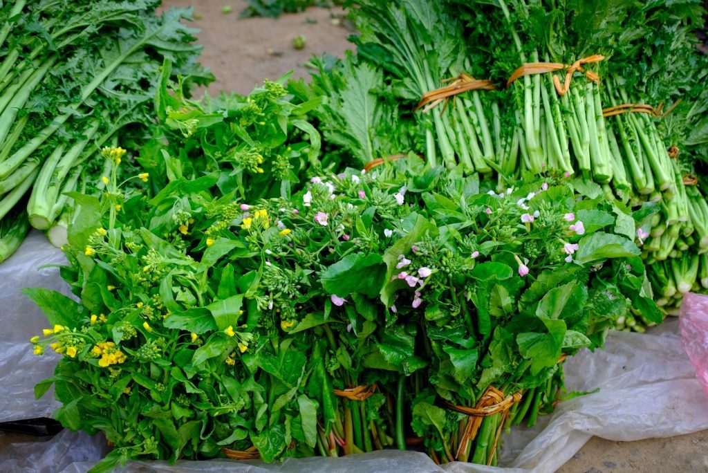 Bundles of fresh green vegetables on display at a vibrant outdoor market in Lào Cai, Vietnam.