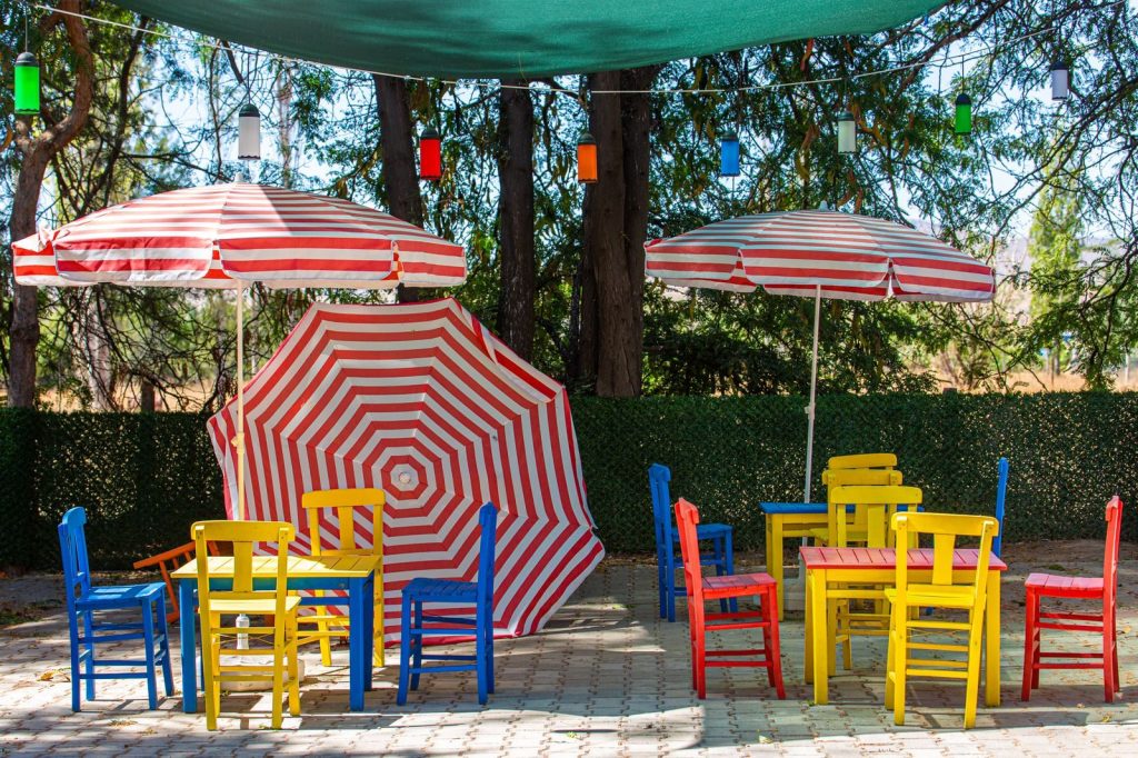 A colorful outdoor café scene featuring bright chairs and striped umbrellas under lighting.