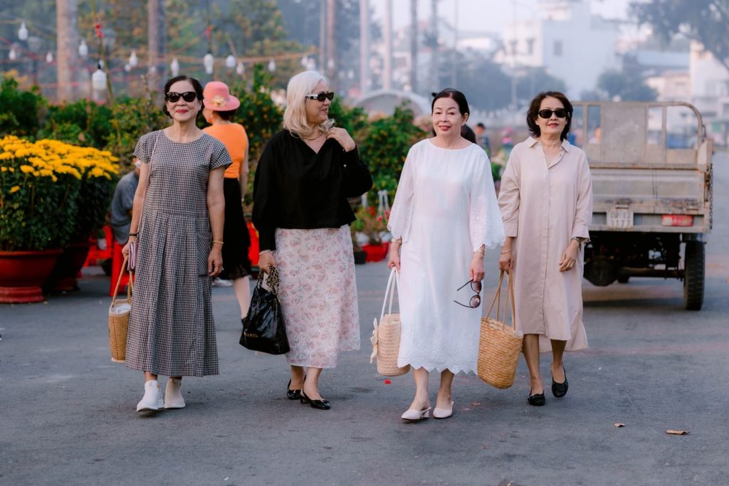 Four senior women enjoying a walk at a vibrant outdoor market in the daytime.