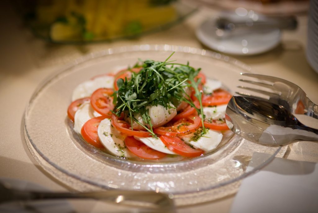 Fresh Caprese salad with mozzarella, tomatoes, and arugula on a glass plate.
