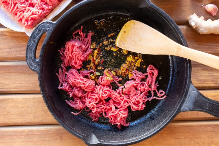 Ground beef frying with garlic in a cast iron skillet on a wooden surface.