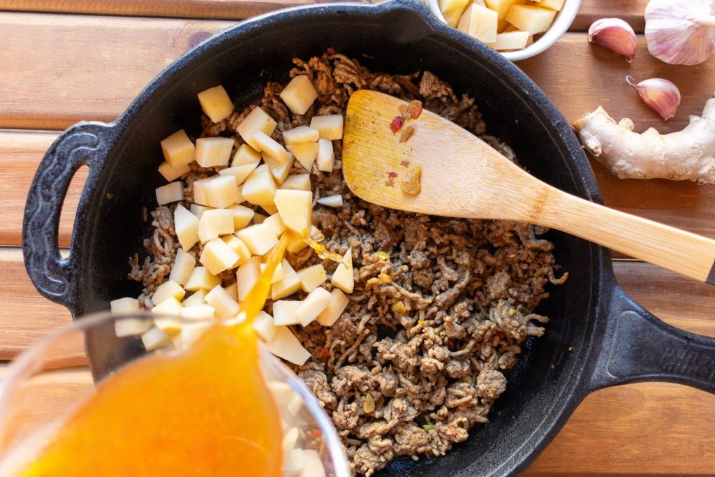 Ground beef and potatoes cooked in a skillet with broth poured in for a hearty meal.