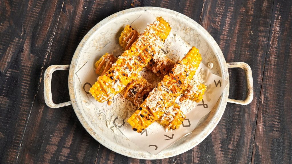 Delicious grilled corn topped with cheese and spices on a rustic plate, perfect for summer meals.