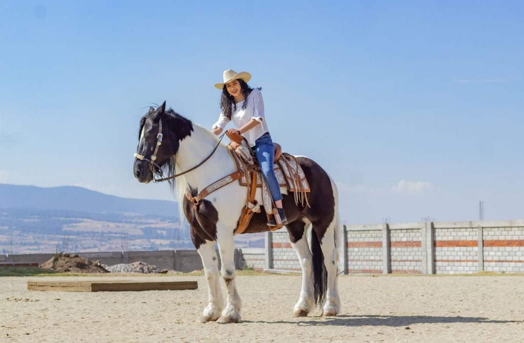 A joyful cowgirl riding a black and white horse outdoors on a sunny day.