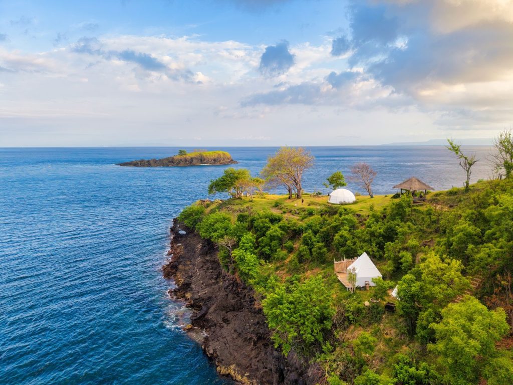 Stunning aerial shot of a lush coastal landscape with tents on a cliff in Bali, Indonesia.