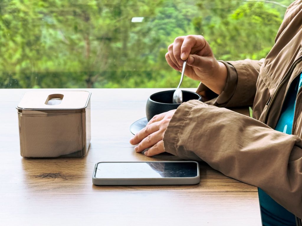 A person enjoys a warm drink at a cozy cafe table with a scenic view.