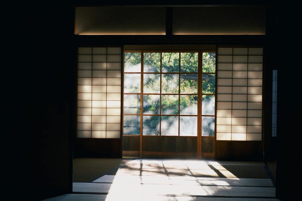 Tranquil Japanese room with traditional shoji screens, diffused sunlight, and a glimpse of nature outside.
