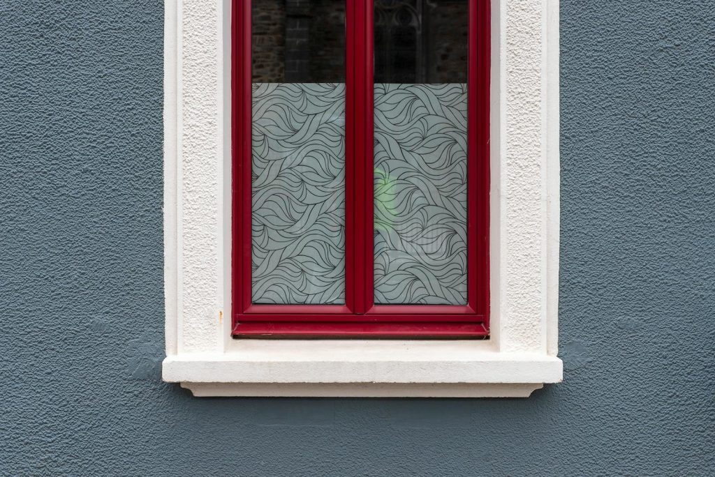 A stylish red-framed window with frosted glass against a textured blue wall.