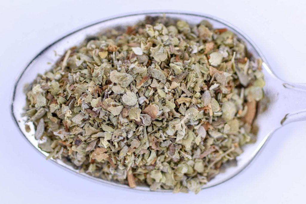 Detailed image of marjoram seasoning in a metal teaspoon, perfect for culinary uses.