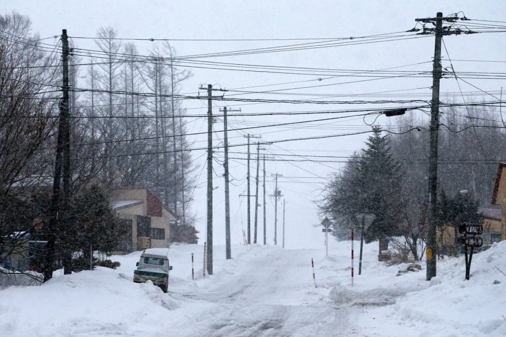 A quiet snowy street lined with power lines and houses in winter.