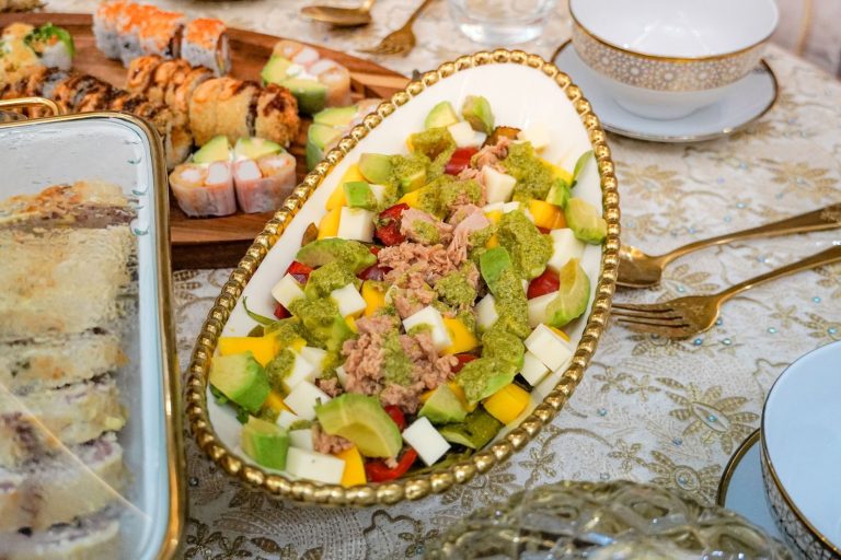 A vibrant dining table featuring sushi rolls and a fresh avocado salad, elegantly arranged.