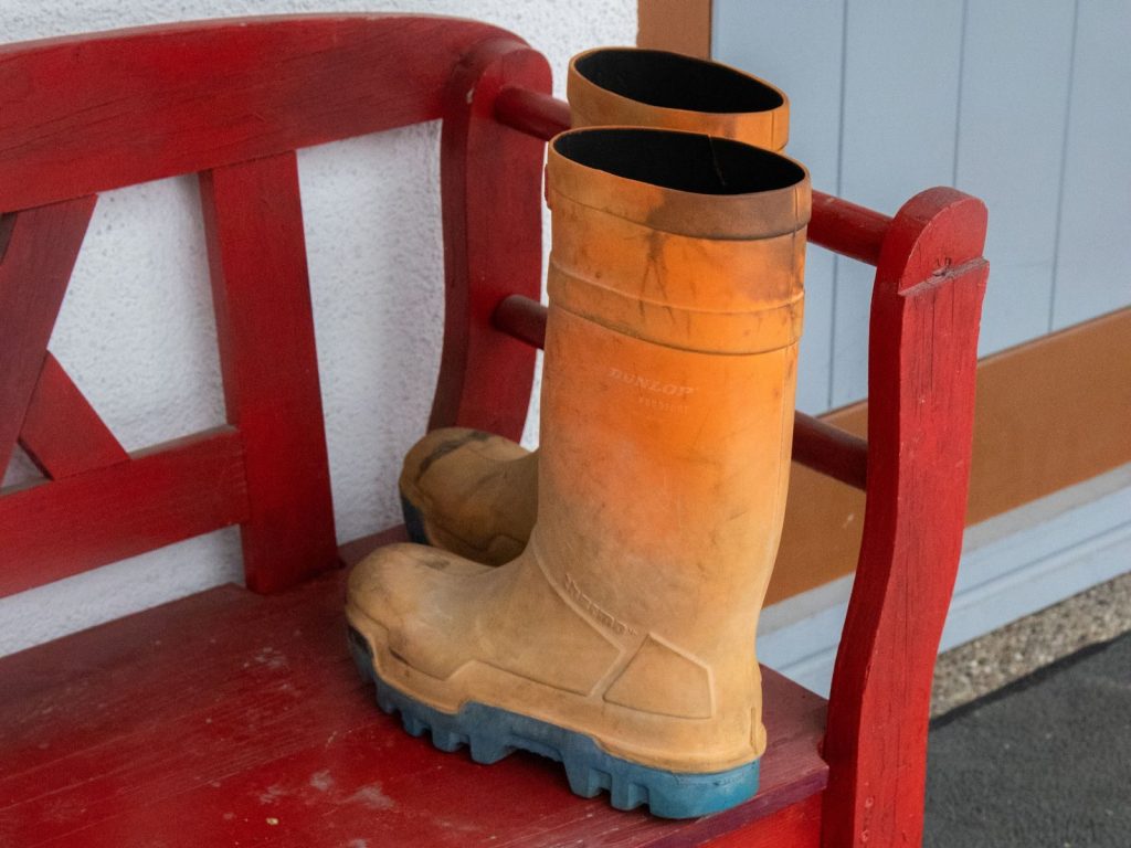 Orange rubber boots resting on a vibrant red bench by a doorway, suggesting rainy weather.