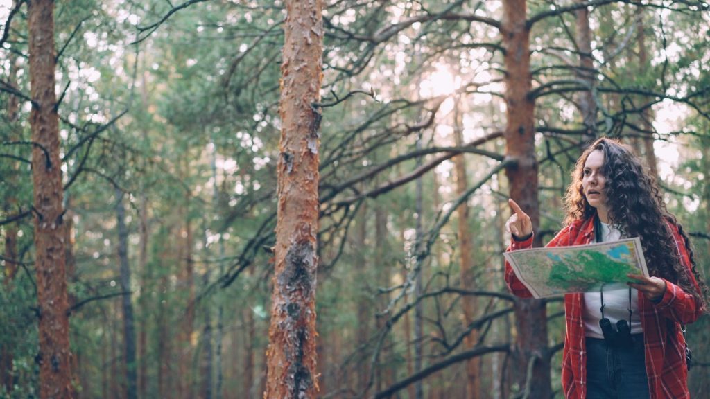 A woman in a red flannel shirt uses a map while navigating a dense forest.