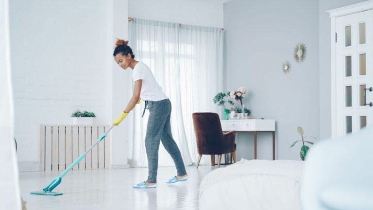 A woman cleaning a bright, modern living room with a mop, creating a clean, welcoming space.