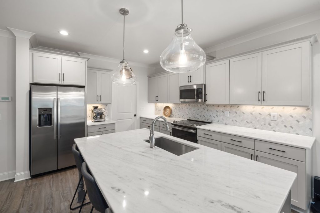 Stylish modern kitchen featuring a marble island, white cabinets, and elegant pendant lighting.