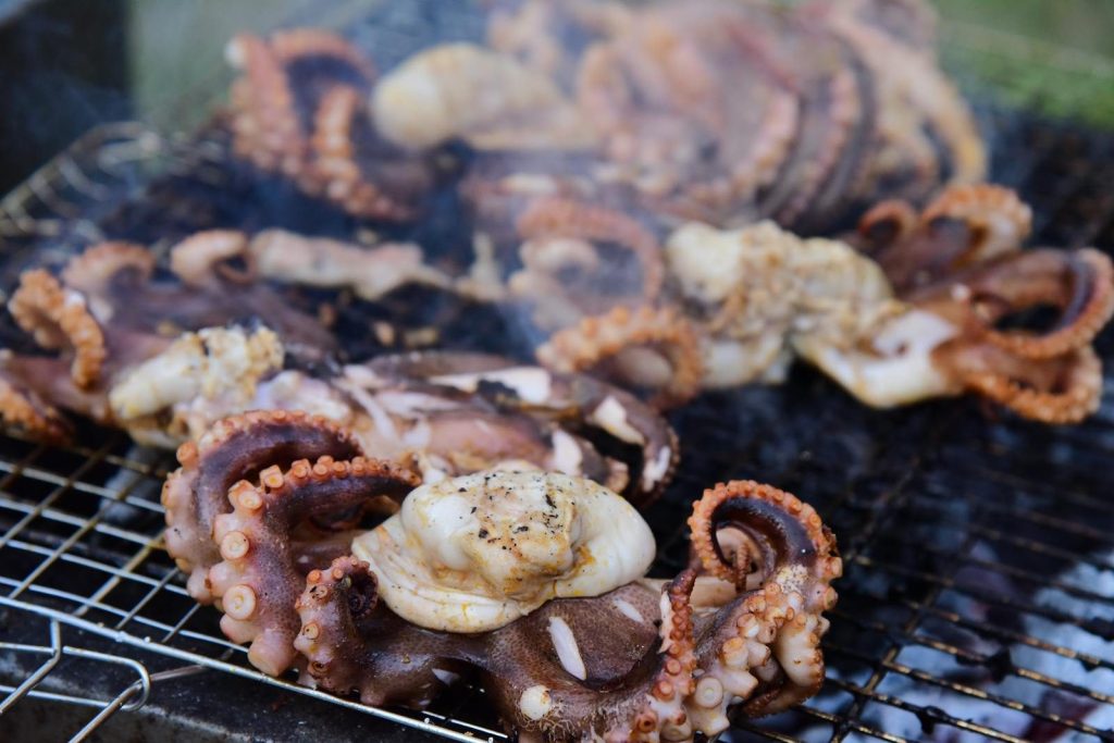 Delicious grilled octopus tentacles sizzling on an outdoor barbecue grill in summer.