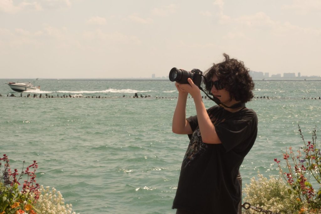 A person photographing a tranquil seaside scene with a DSLR camera on a sunny day.