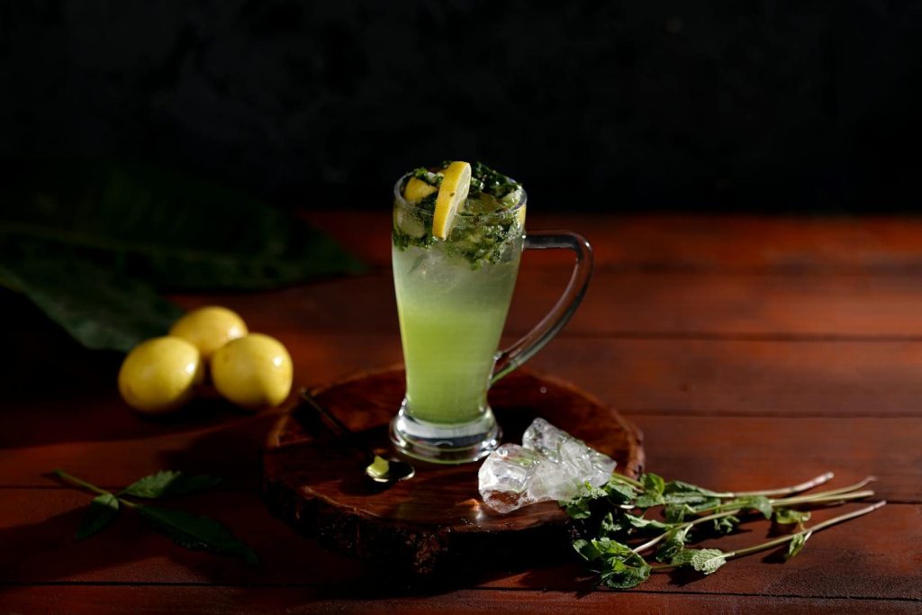 Inviting mint lemonade in a glass with fresh lemons and ice cubes on a wooden table.