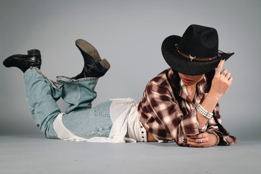 Stylish woman in plaid shirt and jeans with cowboy hat posing indoors.