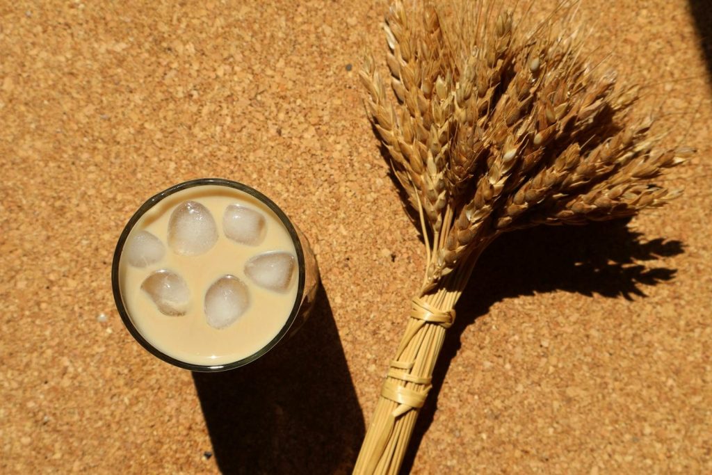 A top-down view of iced coffee and wheat sheaves on a cork surface.